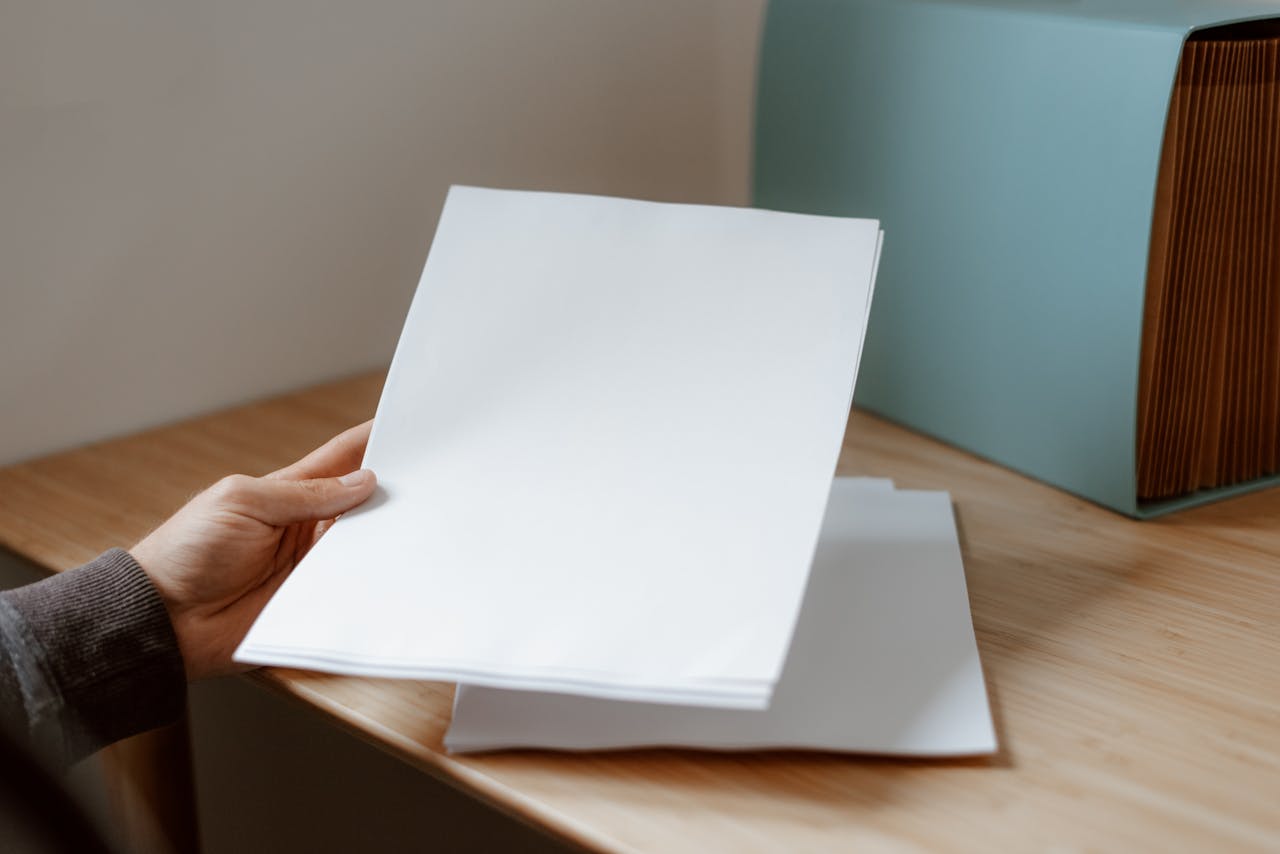 Crop anonymous person demonstrating empty sheet of paper against wooden table with folder for documents